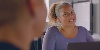 Woman in purple shirt smiles with her laptop in front of her