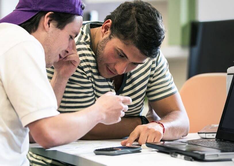 Alumnos trabajando en equipo y señalando a unos papeles y a un teléfono o tablet sobre la mesa.