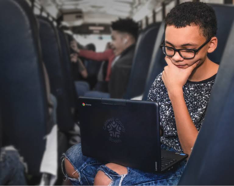 통학 중에 자리에 앉아서 Chromebook 기기에 집중하고 있는 안경 쓴 학생