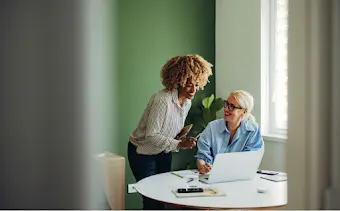 Two women huddled over one laptop sharing and discussing work.