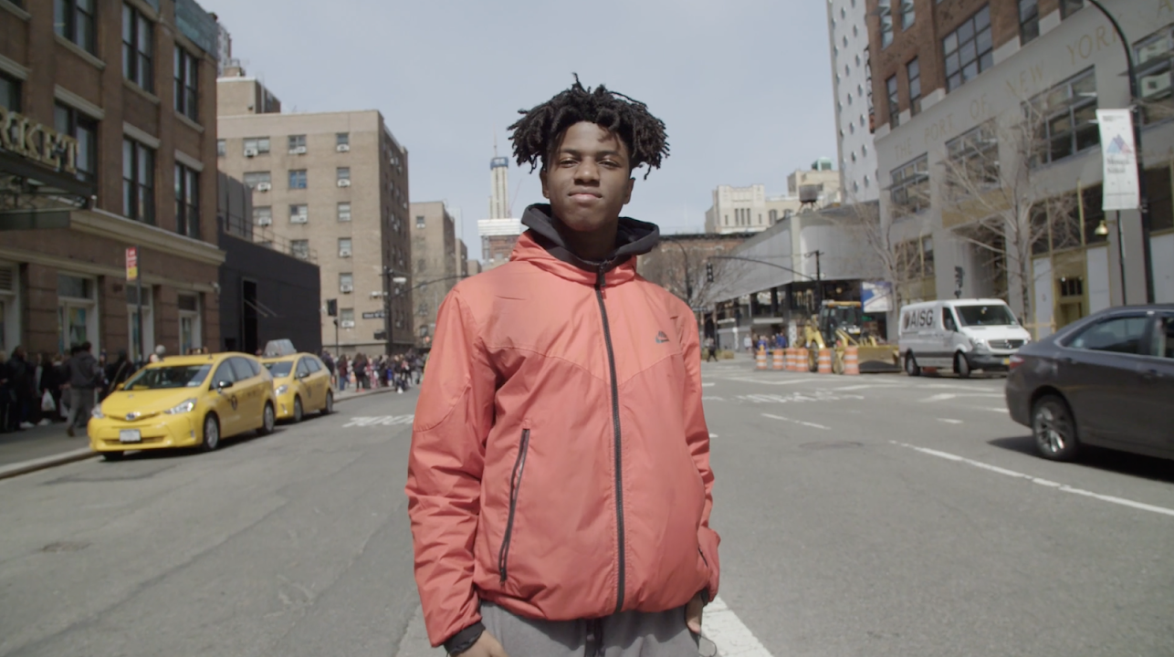 Young black male looks proudly into camera with city skyline in the background.